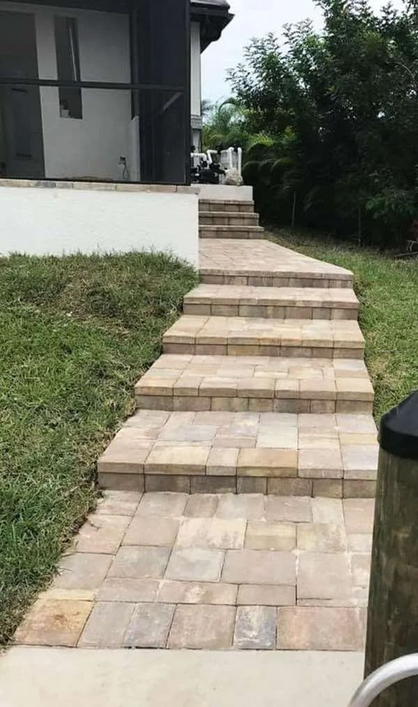 Paved stone steps leading to a house, surrounded by grass and greenery.
