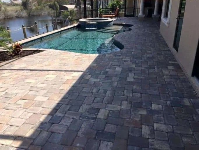 Elegant patio with paver stones, pool, spa, and scenic waterfront view. Ideal for outdoor living.