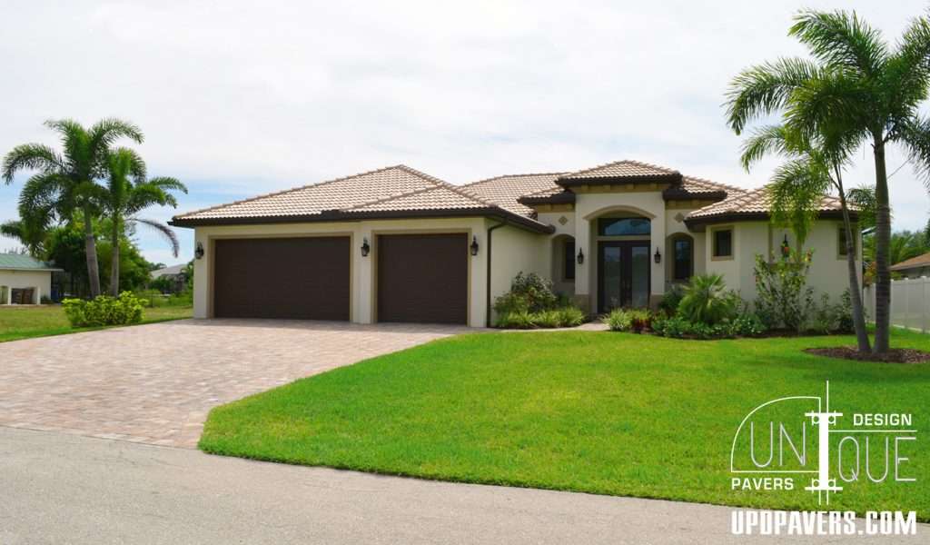 Modern residential home with paver driveway, tropical landscaping, and double garages.