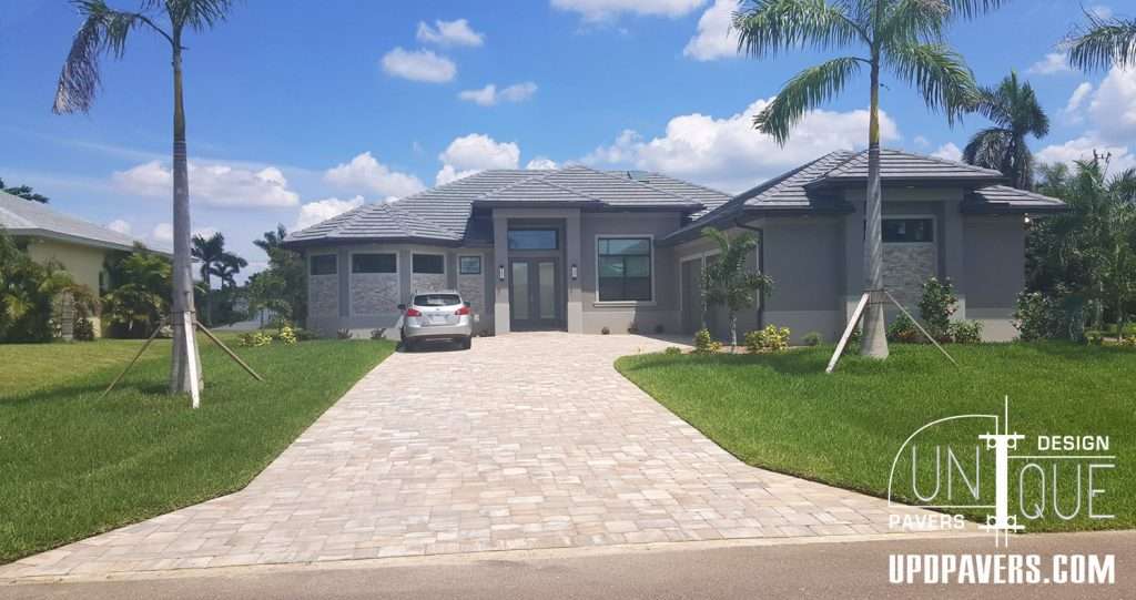 Modern home exterior with paver driveway, palm trees, and landscaped yard. Unique design features.