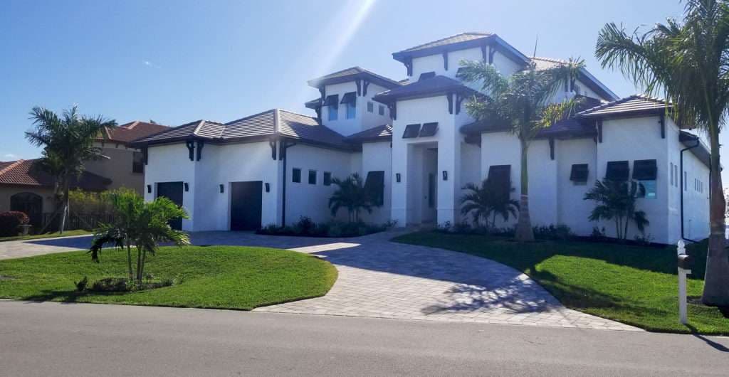 Modern white luxury house with a landscaped yard, palm trees, and a circular driveway.