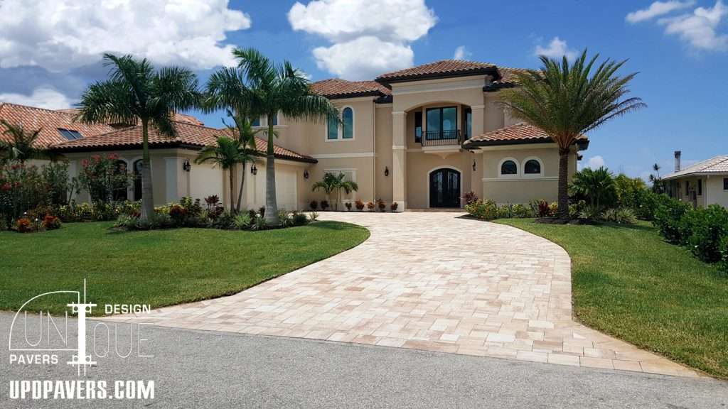 Elegant luxury home with a paved driveway, landscaped yard, and palm trees under a sunny sky.