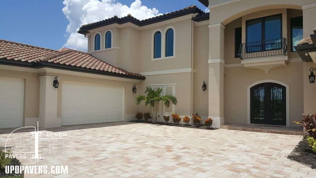 Luxury home exterior with cobblestone driveway and tropical landscaping.