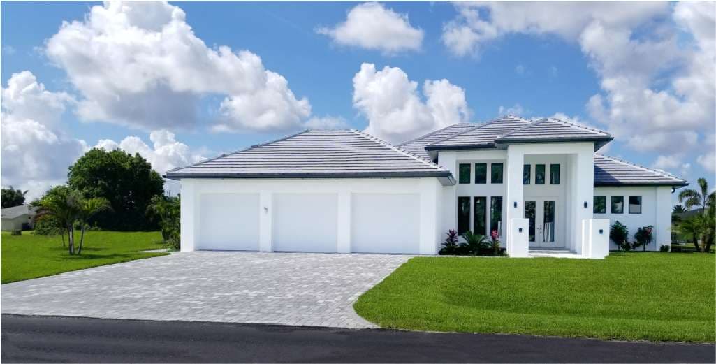 Modern white luxury home with three-car garage and lush green landscaping under a blue sky.