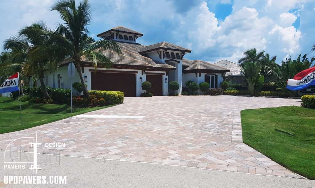 Elegant home with paver driveway, tropical landscaping, and blue sky backdrop.