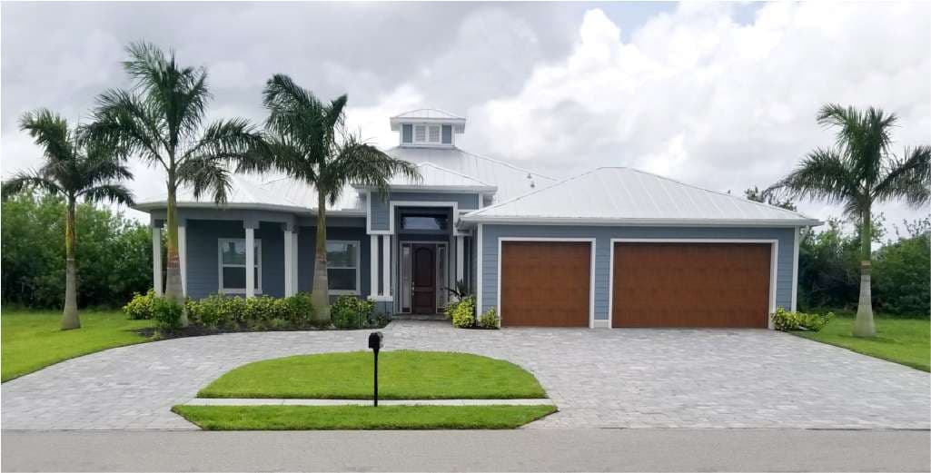 Modern blue house with a metal roof, double garage, and palm trees, set on a landscaped front yard.
