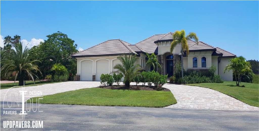 Stylish home with palm landscaping and decorative paver driveway under clear blue skies.