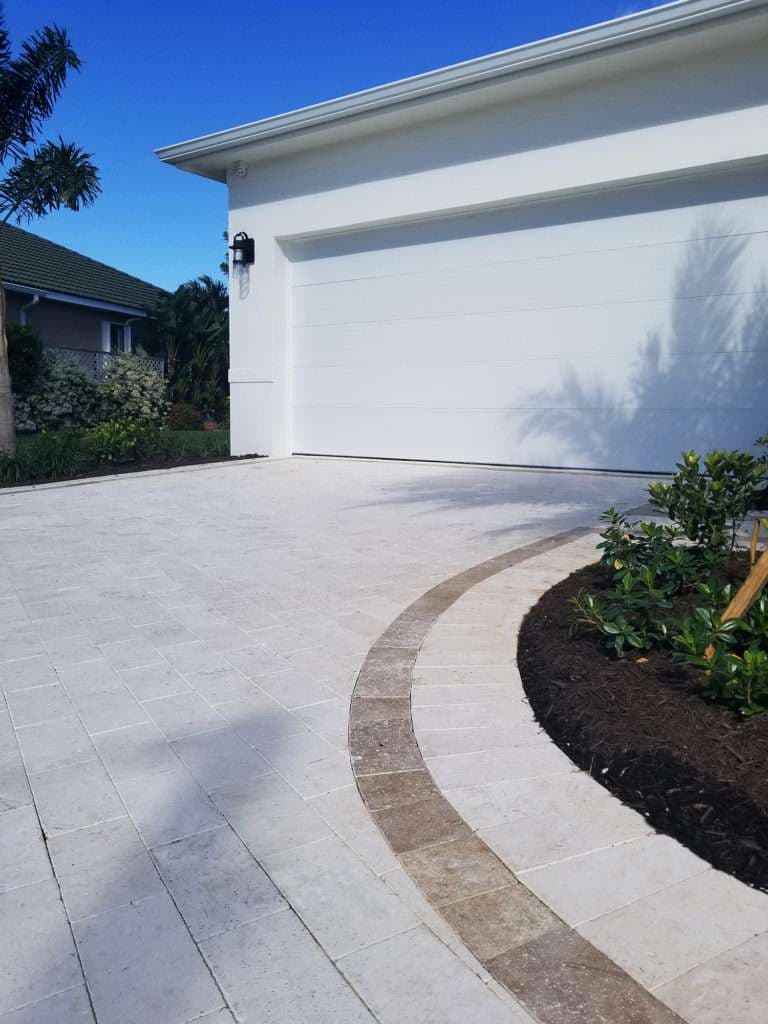Modern driveway design with paver stones, adjacent to landscaped plants and a white garage door.