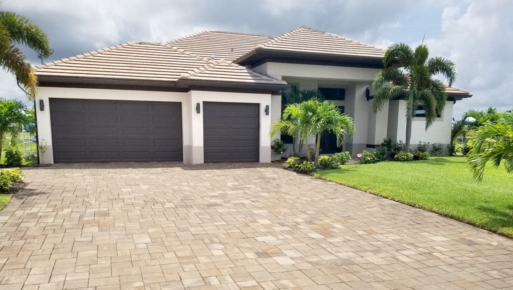 Modern single-family home with three-car garage, lush landscaping, and tile roof.