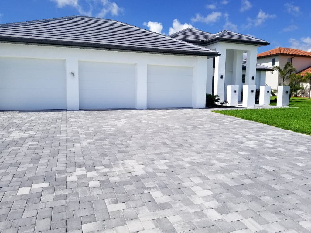 Modern house facade with paver driveway and three garage doors under a clear blue sky.