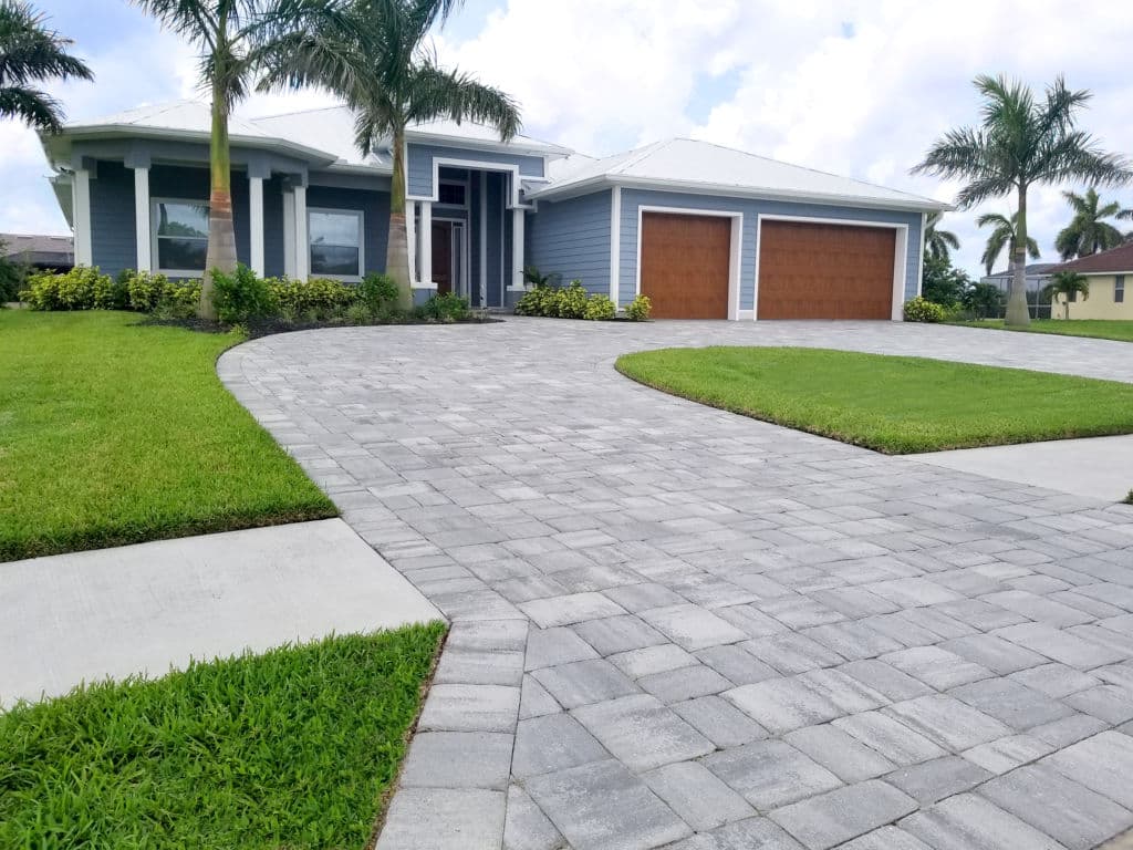 Modern house with two garage doors, landscaped yard, and paved driveway, sunny day.