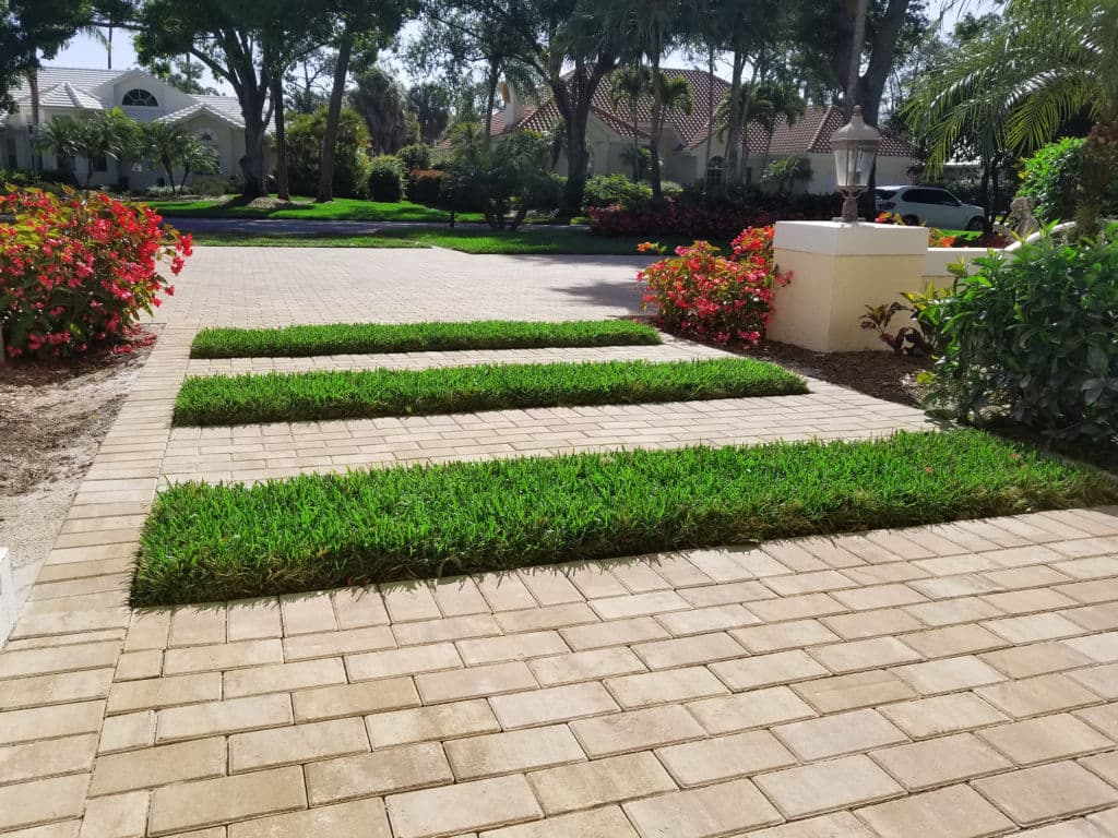 Stylish paved driveway with lush green grass strips and vibrant flowerbeds.
