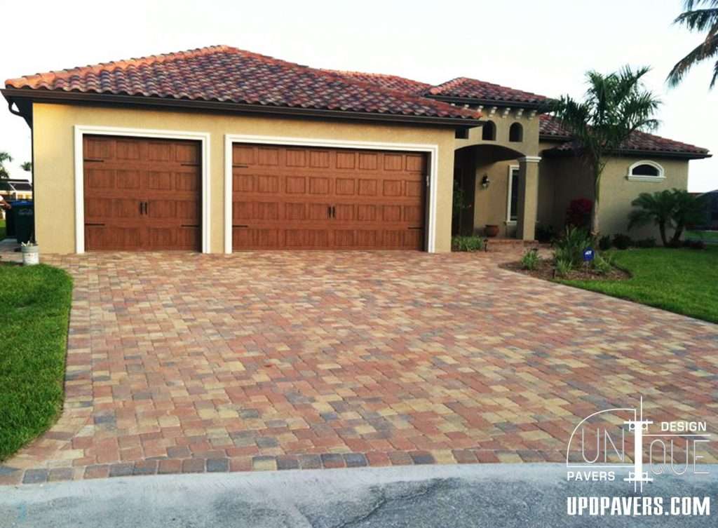 Stylish home with a brick driveway and dual wooden garage doors, surrounded by green landscaping.