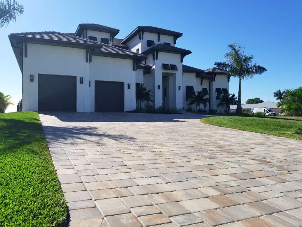 Modern luxury home with a spacious driveway and tropical landscaping under clear blue sky.