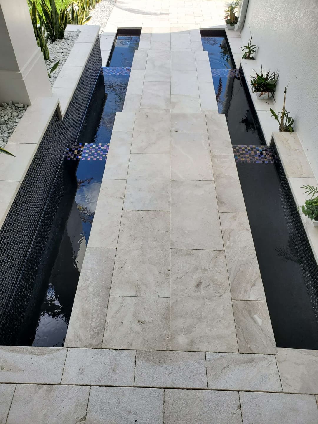 Modern outdoor pathway with water features bordered by sleek landscaping and decorative tiles.