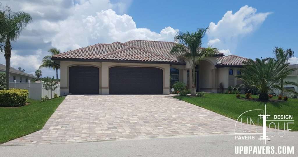 Elegant Mediterranean-style home with paver driveway, palm trees, and clear blue sky.