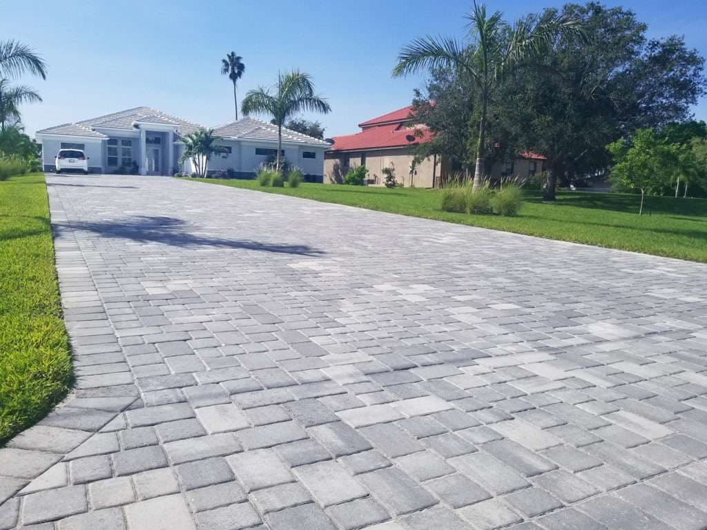Paved driveway leading to modern homes surrounded by lush greenery and palm trees.