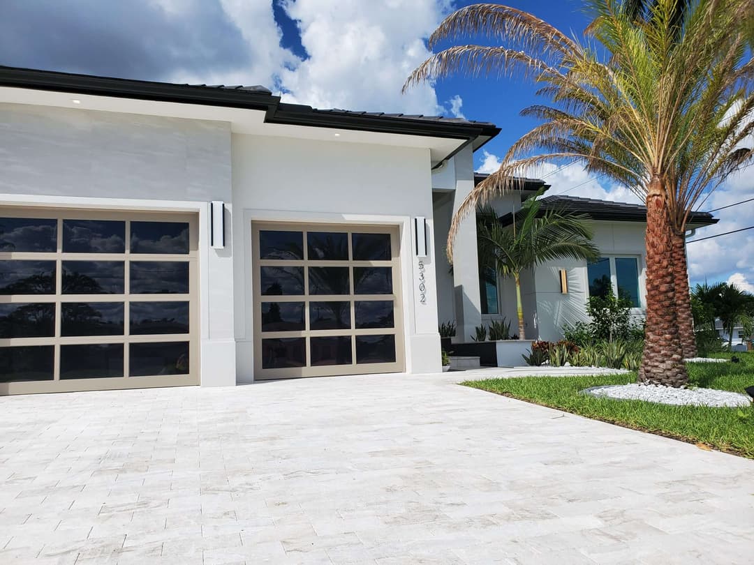 Modern home exterior with palm trees and stone driveway under blue skies.
