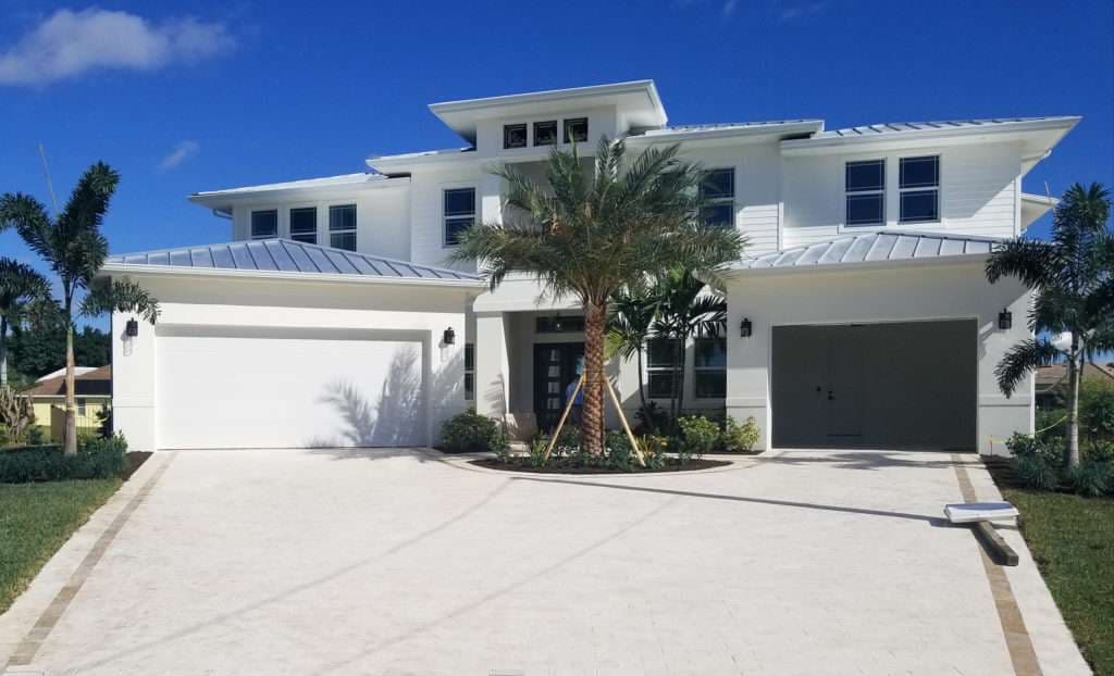 Modern white two-story home with palm trees and a spacious driveway under a blue sky.
