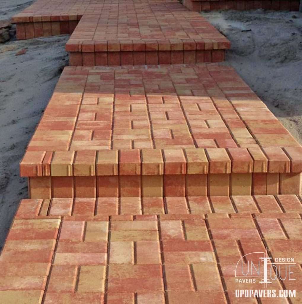 Red and beige interlocking paver walkway leading to a pathway, ideal for landscaping.