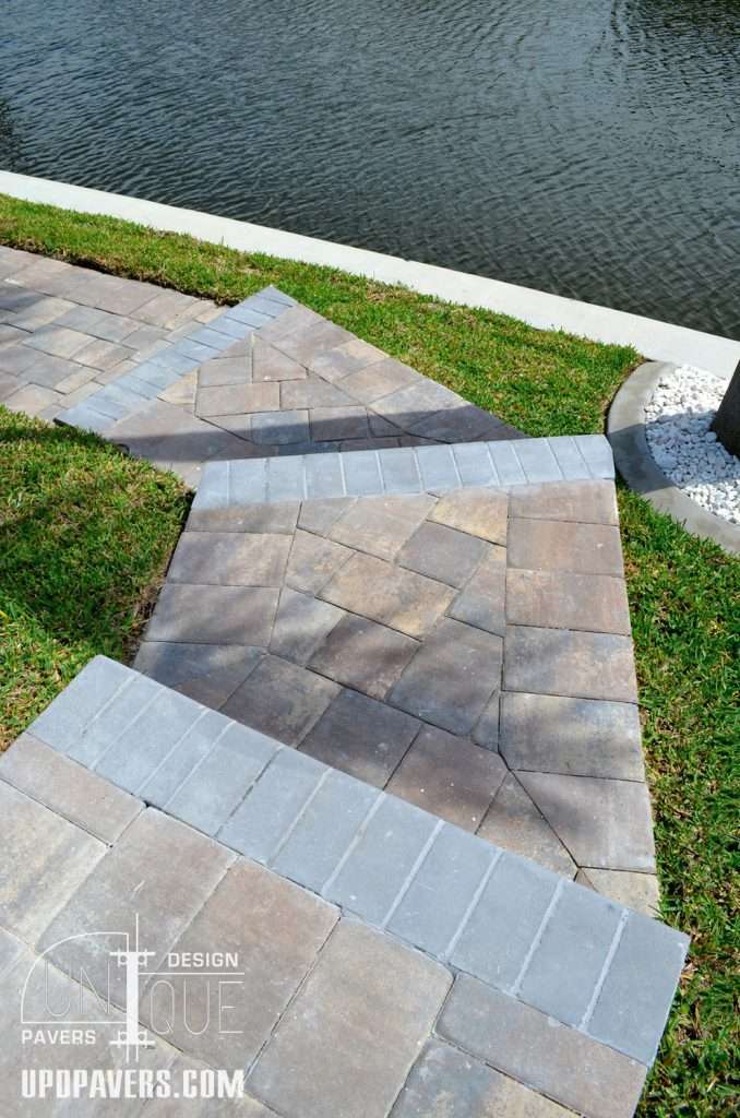 Stylish paver walkway design along water feature with lush green grass.