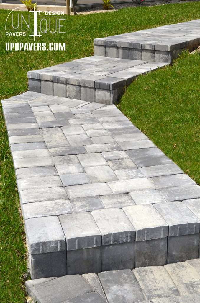 Stylish gray paver walkway curving through green grass for landscaping design.