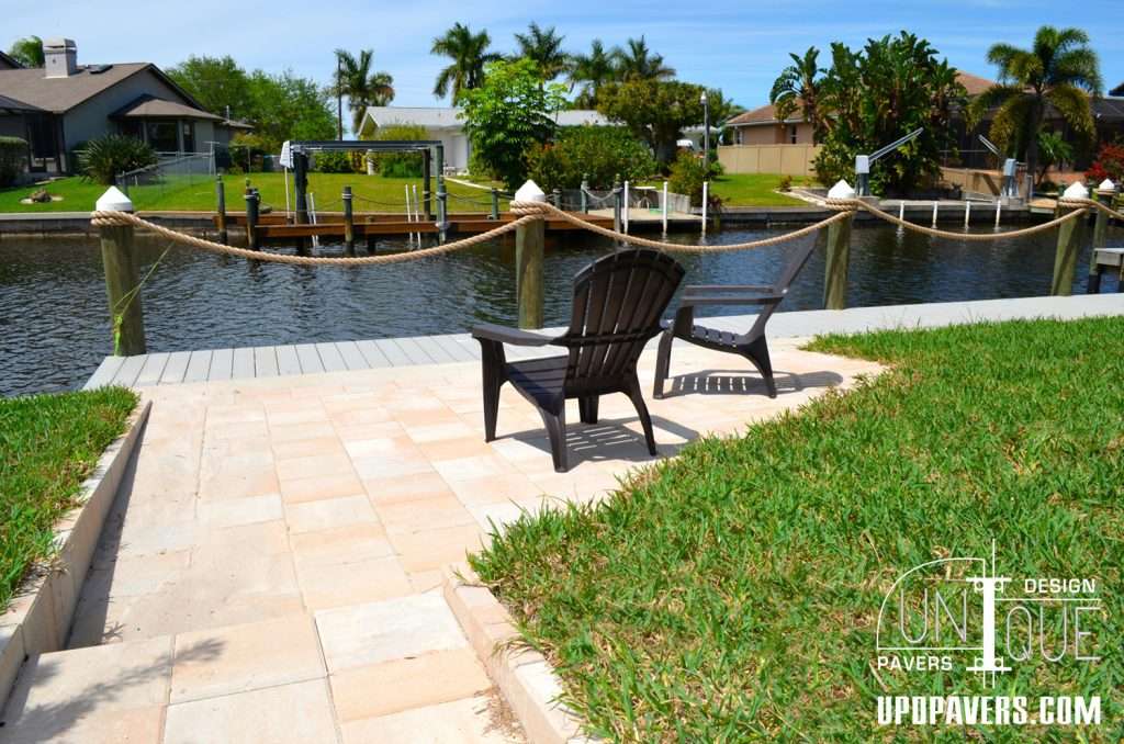Lakeside patio with two chairs, lush grass, and calm water view surrounded by palm trees.
