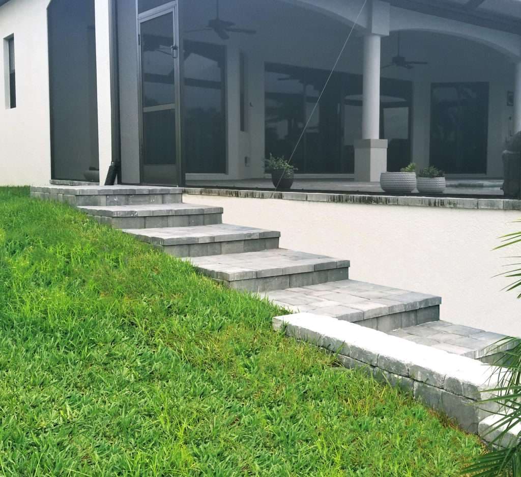 Stone steps lead to a modern home patio surrounded by lush green grass.