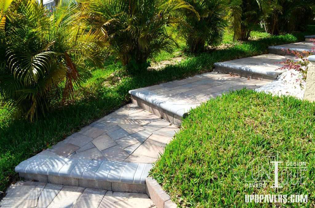 Beautiful paved pathway surrounded by lush green grass and tropical plants.