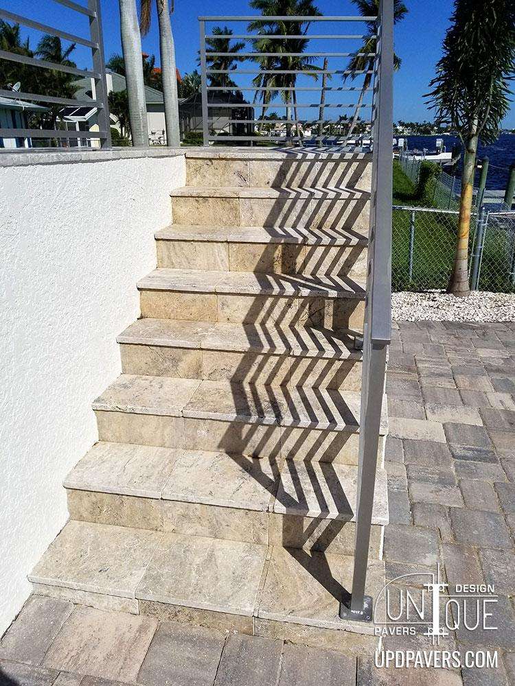 Elegant stone staircase with shadows, surrounded by palm trees and a scenic waterfront.