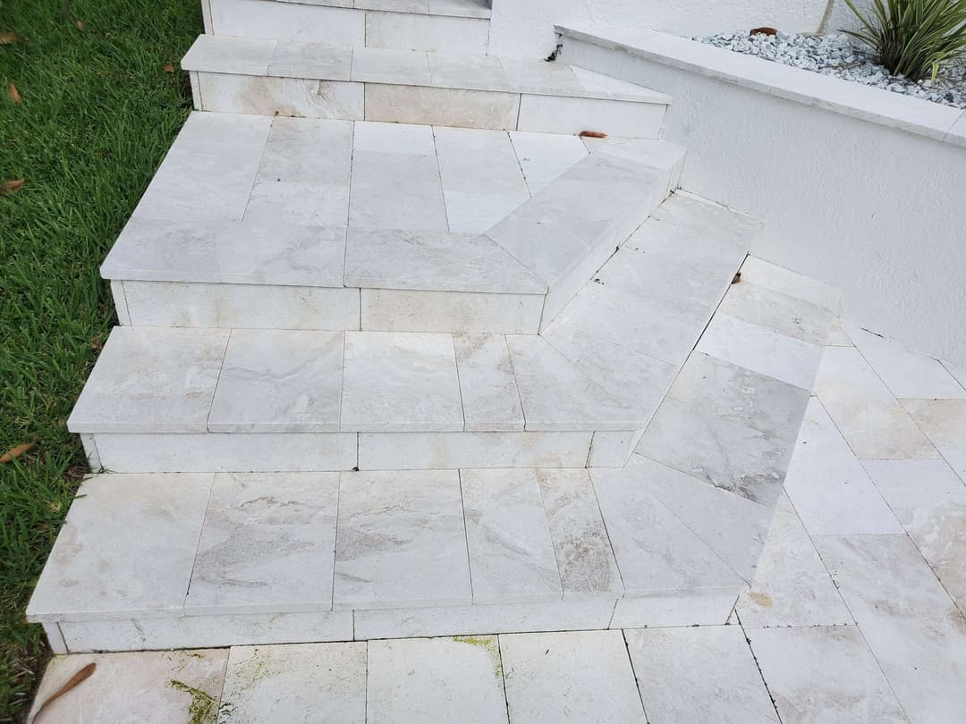 Marble staircase with smooth tiles leading up to a white wall in a landscaped garden.