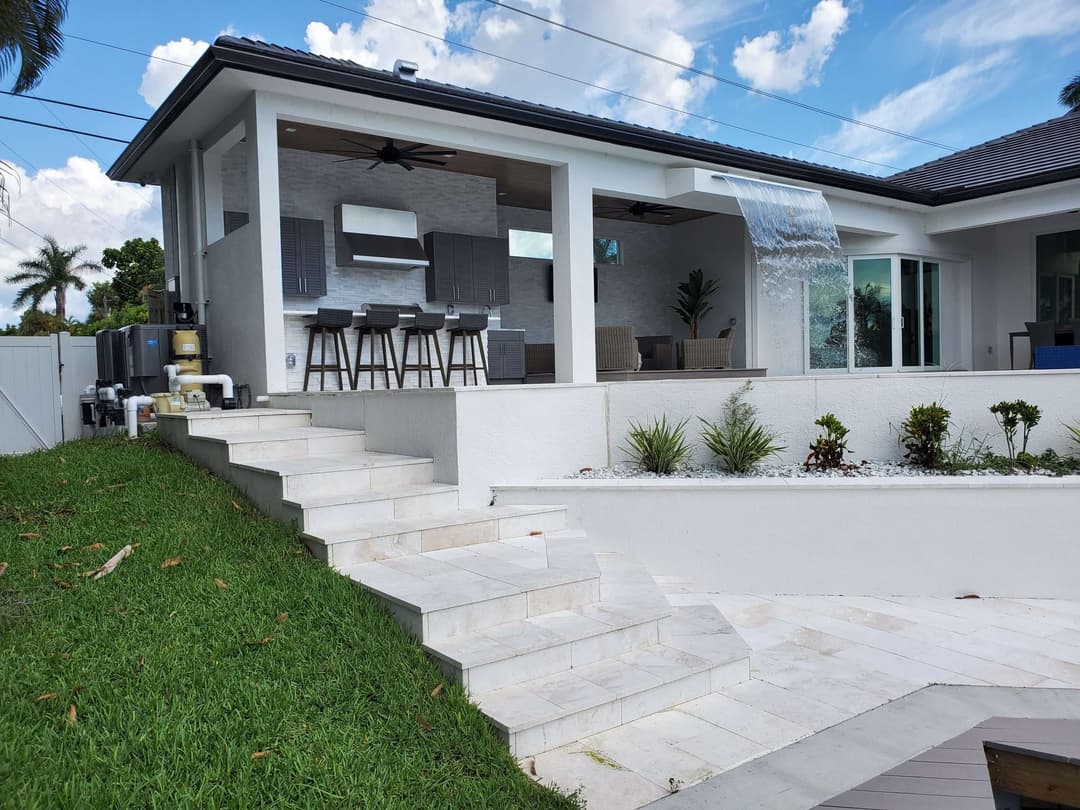 Modern home exterior with stairs, patio furniture, and lush landscaping. Bright sunny day.