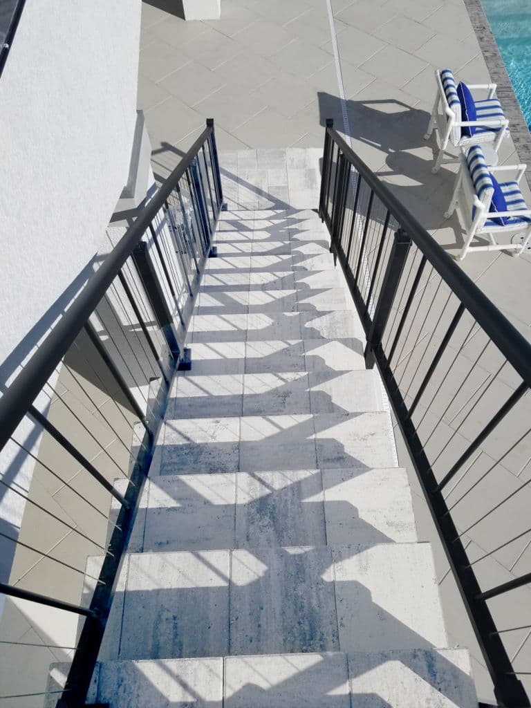 Staircase with shadows leading down to a pool area and lounge chairs.