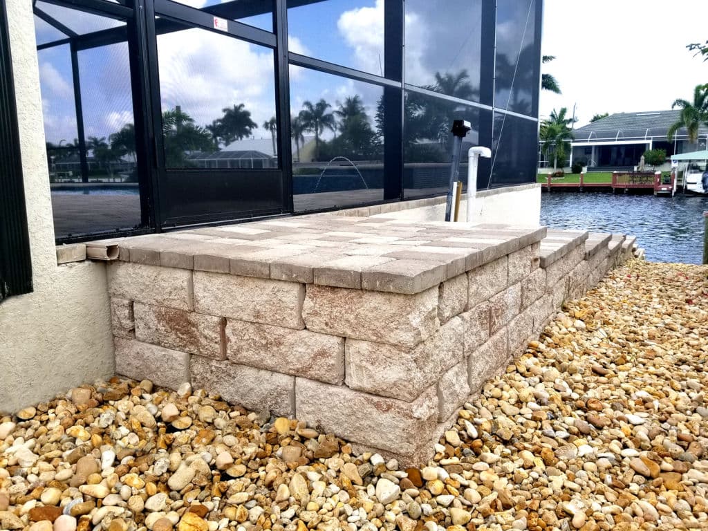 Paver stone patio with retaining wall by water, surrounded by landscaping stones.