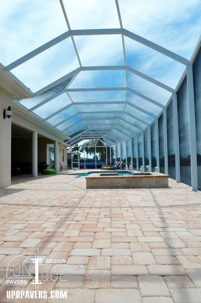 Modern pool enclosure with paver patio, clear blue sky, and lounging chairs for relaxation.