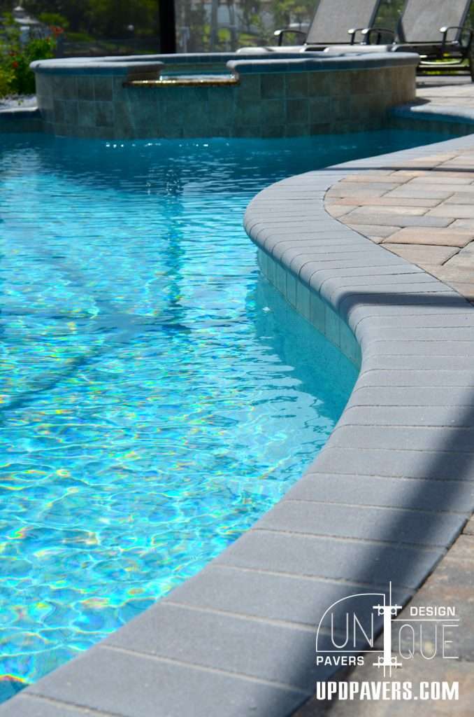 Elegant poolside with shimmering water and modern paver design, featuring a spa area.