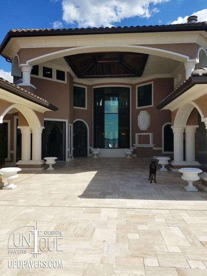 Luxurious entrance of a modern home with elegant architecture and a dog standing on a paver patio.