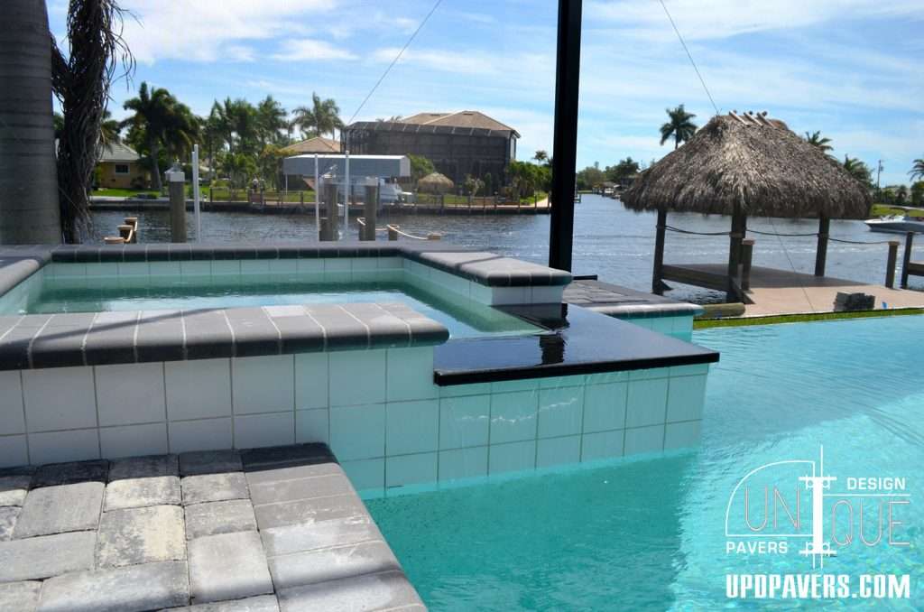 Luxury pool and spa with pavers overlooking a scenic waterfront view. Tropical landscaping.