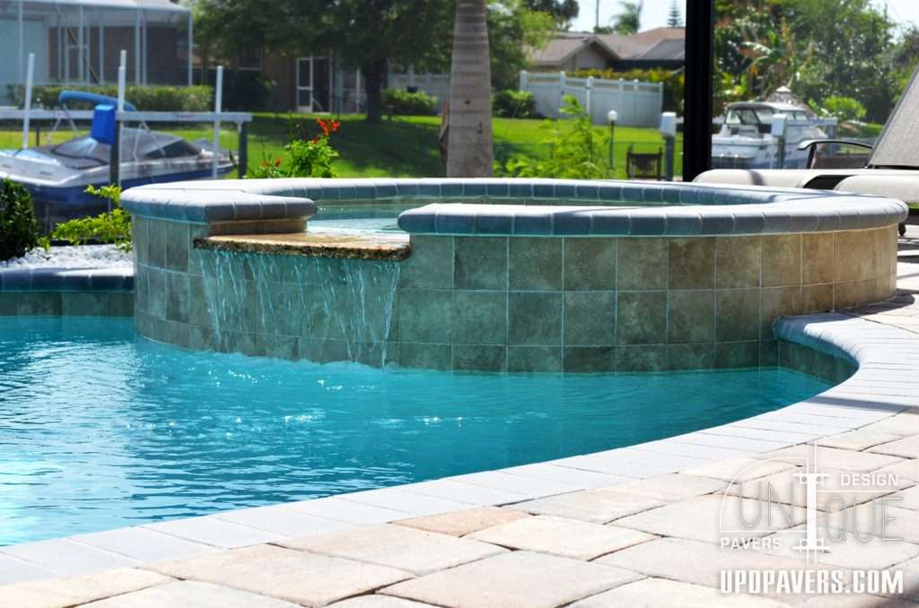 Luxury pool design with a spa and waterfall feature under clear blue skies.