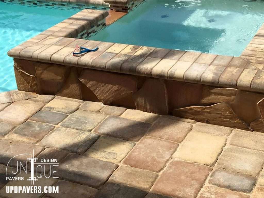 Paver design around swimming pool with blue flip-flops resting on the edge.