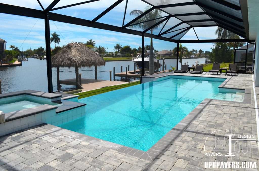 Modern outdoor pool with pavers, spa, and waterfront view in a tropical setting.