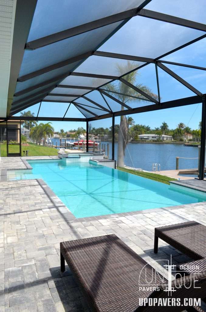 Stunning backyard pool with paver patio and water view under a screened enclosure.