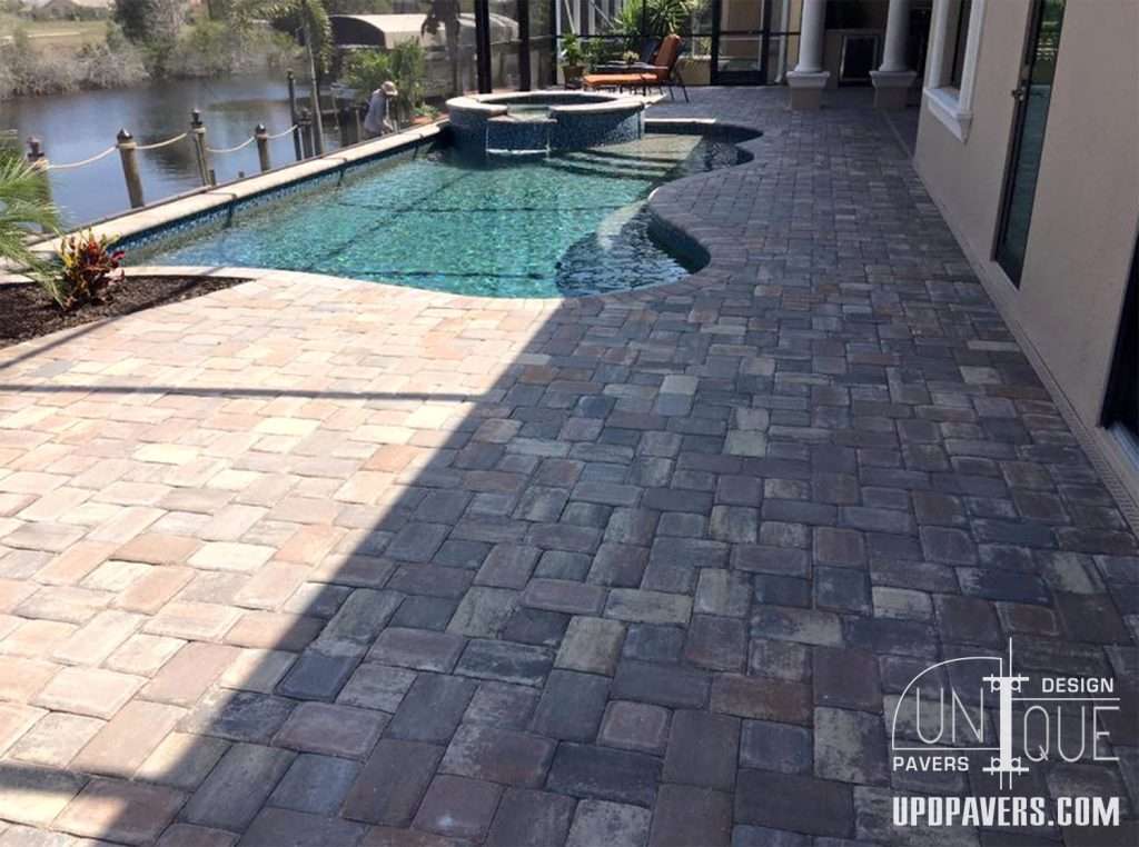 Beautiful patio with paver stones surrounding a pool and spa by Unique Pavers Design.