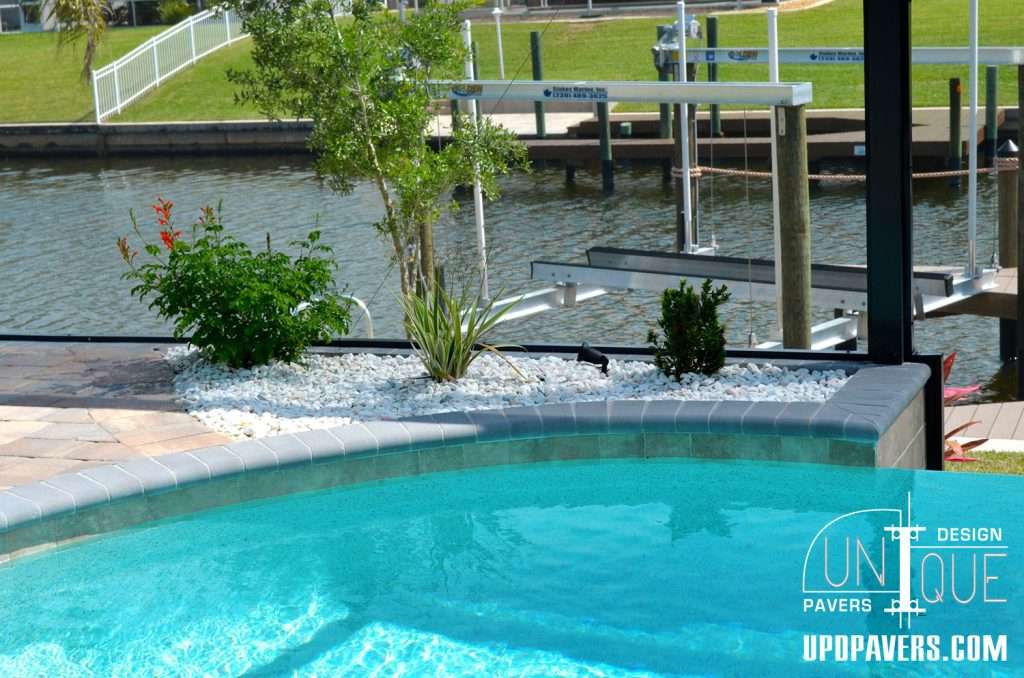 Clear blue swimming pool with lush plants, waterfront view, and modern patio design.