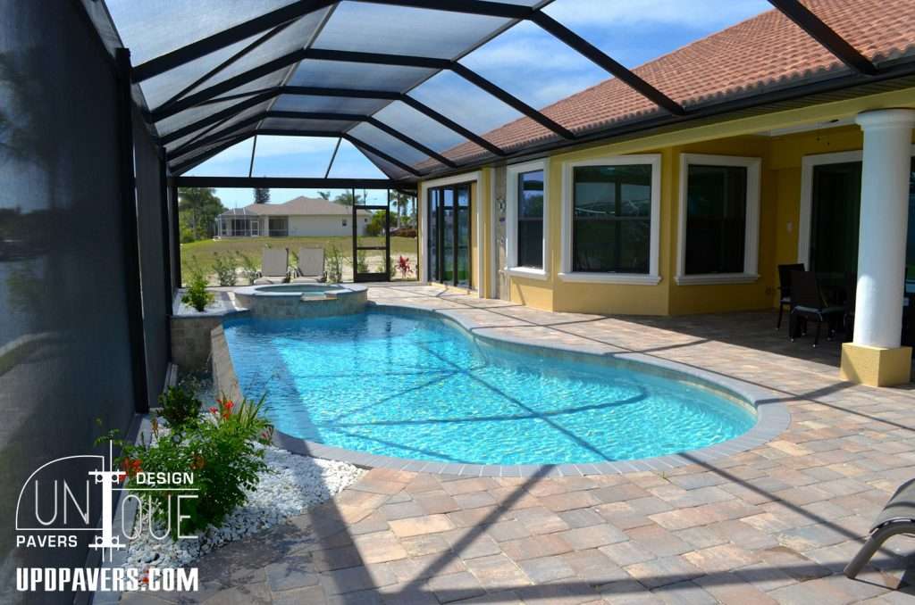 Modern outdoor pool with paver patio and screened enclosure, featuring a spa and garden.