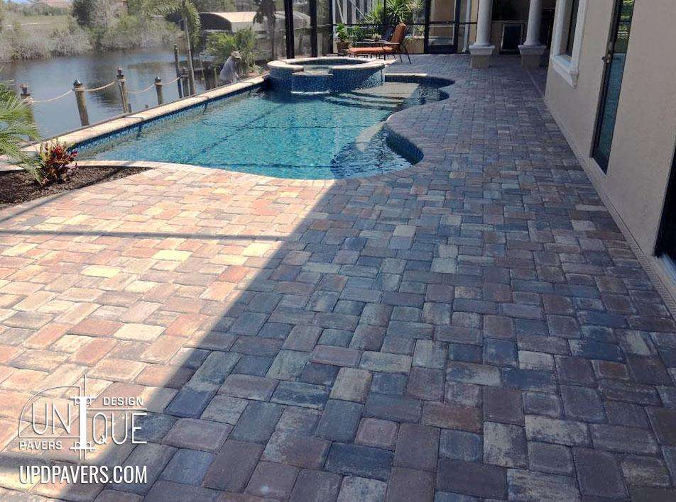 Paver patio by a pool with spa overlooking water, showcasing elegant outdoor design.