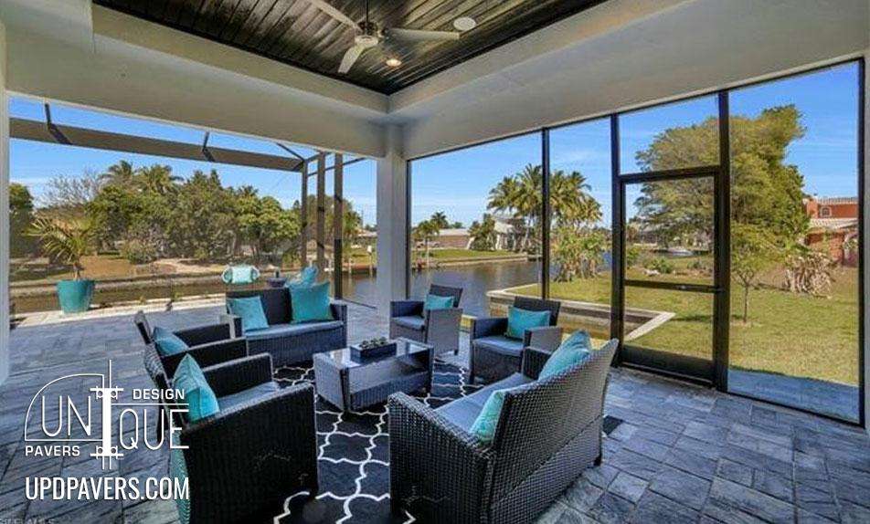 Modern outdoor living space with seating, pavers, and a view of lush greenery.