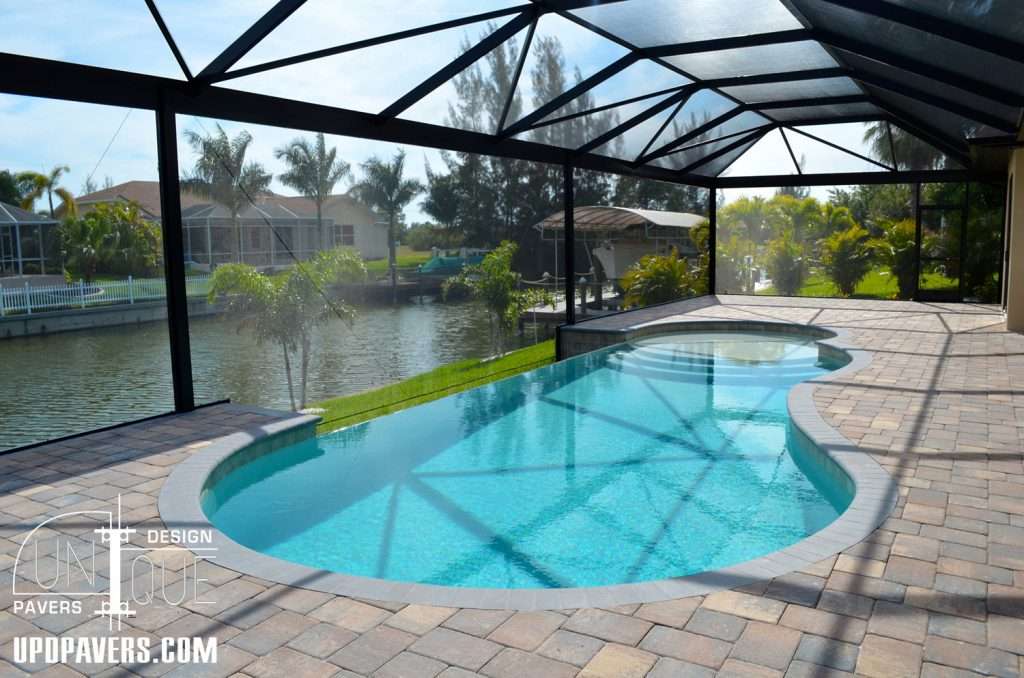 Elegant pool with pavers in a screened lanai overlooking a tranquil waterfront view.