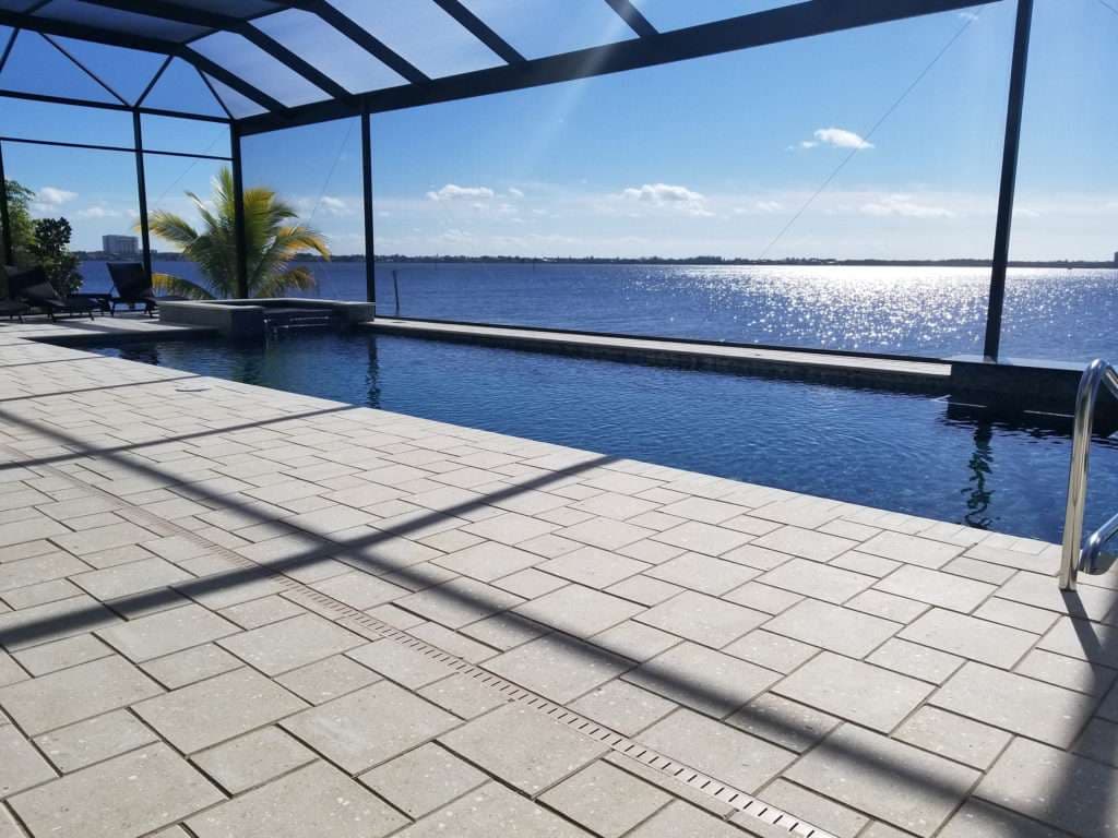 Infinity pool with a view of the shimmering lake and blue sky, surrounded by patio stones.