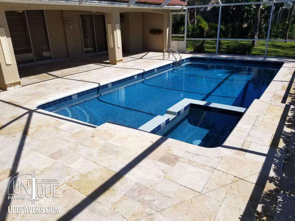 Luxury backyard pool with spa, surrounded by elegant stone patio and lush greenery.